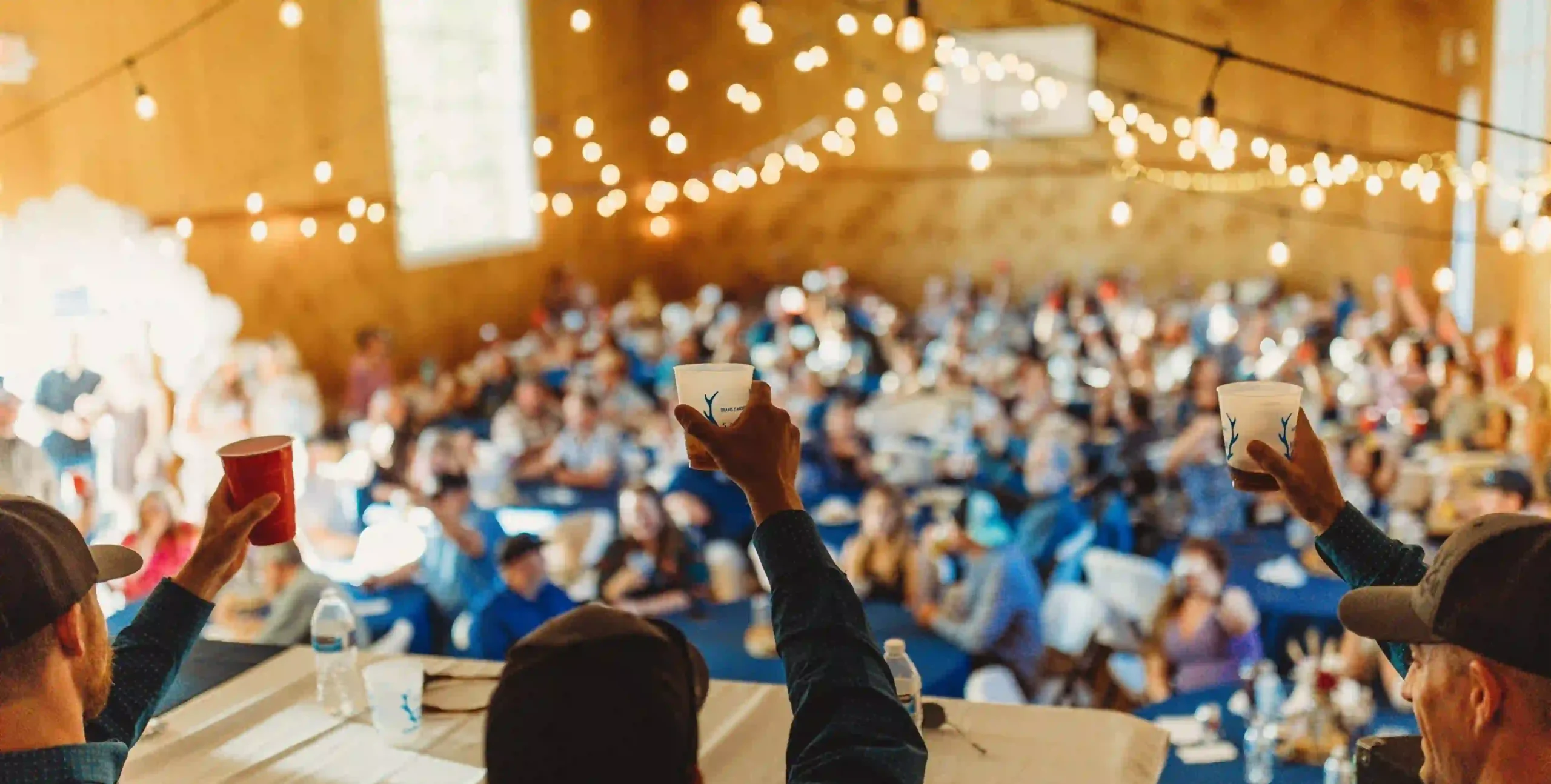 Conference attendees raise glasses in celebration at large indoor networking event