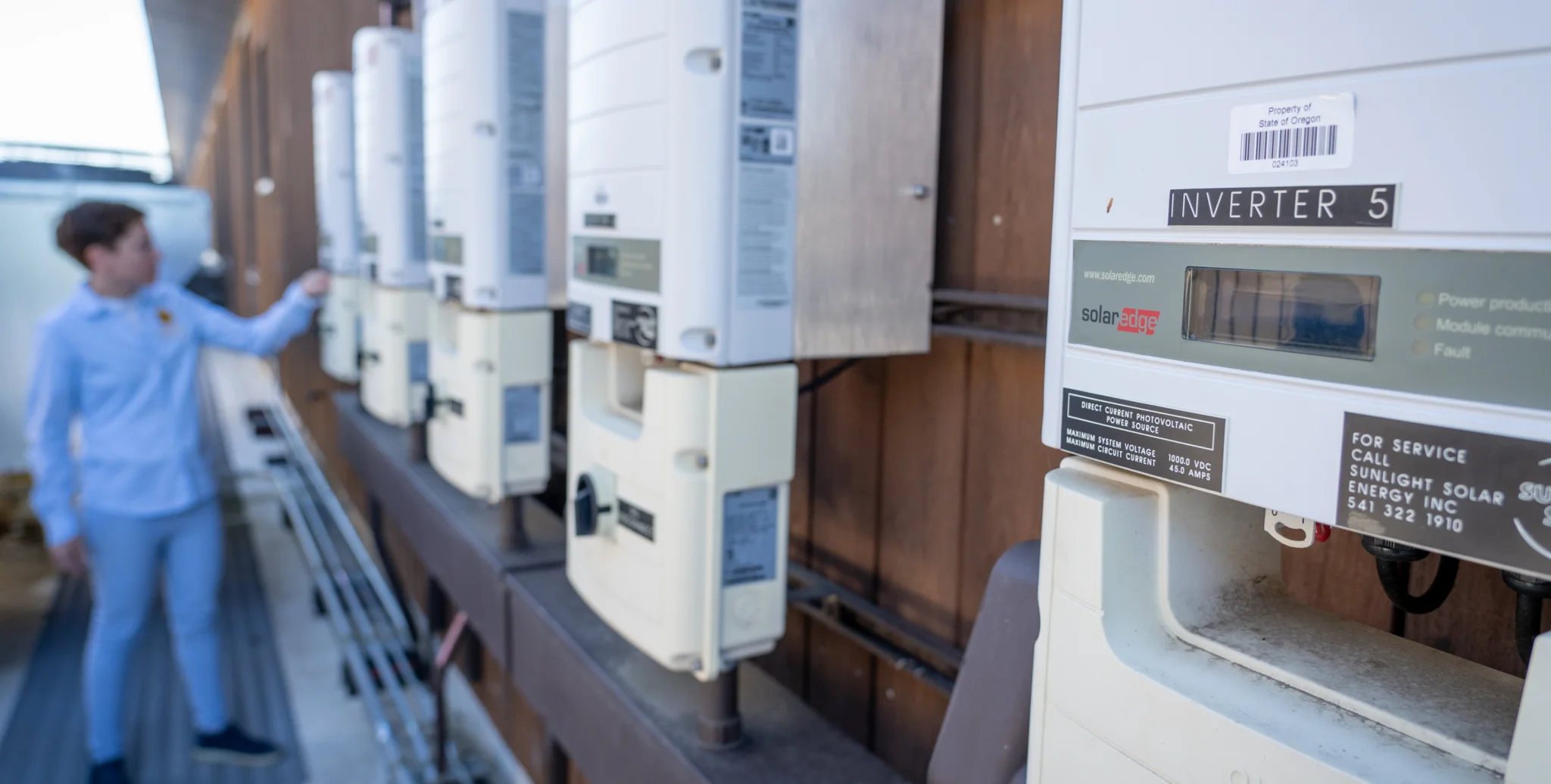 Technician inspects row of solar inverters during on-site photovoltaic system maintenance