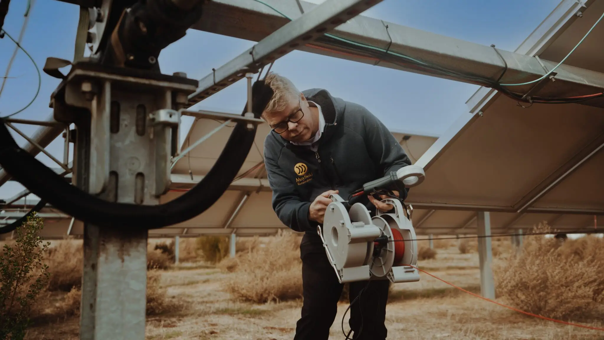 Renewable energy engineer inspects solar tracking equipment beneath ground-mounted panels