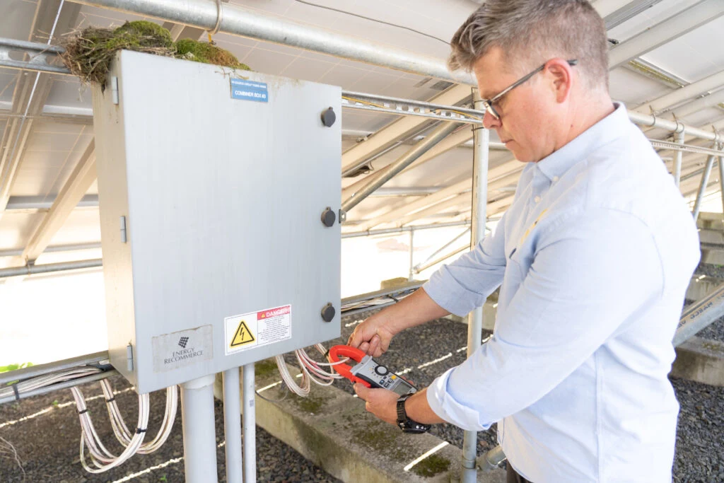 Technician testing solar electrical panel with clamp meter during rooftop system inspection
