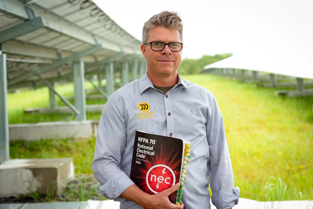 Founder of Mayfield Renewables, Ryan Mayfield holding a NEC book